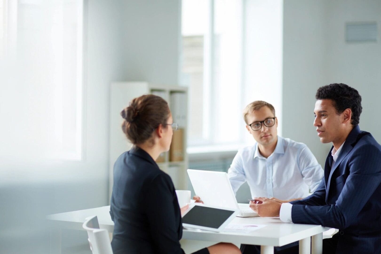 Three people sitting at a table with one of them holding a laptop.